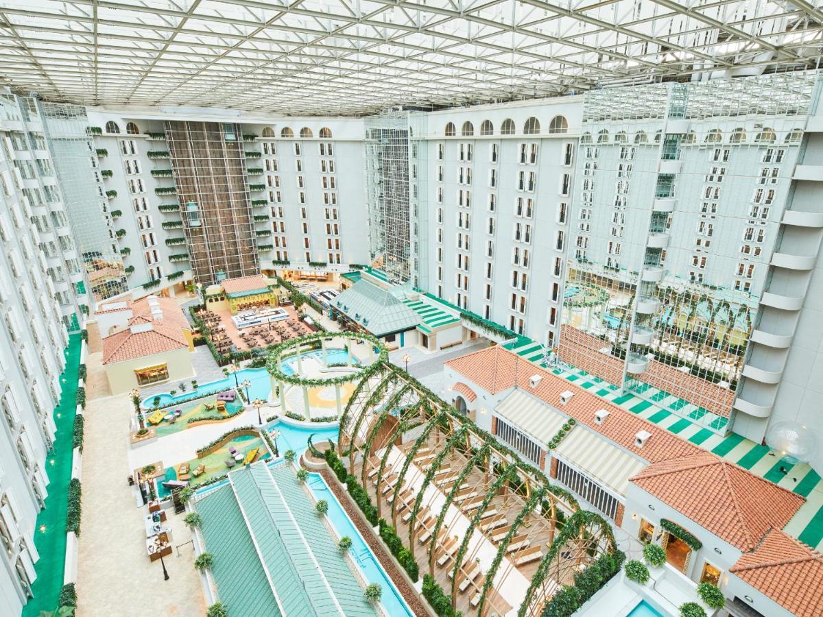 Grand Nikko Tokyo Bay Maihama Hotell Urayasu Exteriör bild The photo shows a large indoor space, likely a hotel or resort atrium. The area features multiple levels of buildings surrounding a central courtyard. This courtyard includes various amenities such as pools, landscaped gardens, and recreational areas