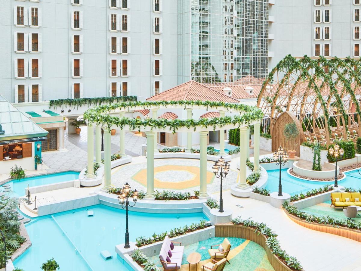 Grand Nikko Tokyo Bay Maihama Hotell Urayasu Exteriör bild The photo shows a beautifully landscaped outdoor area, likely part of a resort or hotel. It features a central circular structure supported by white columns, decorated with greenery. Surrounding this structure are several swimming pools or water feat