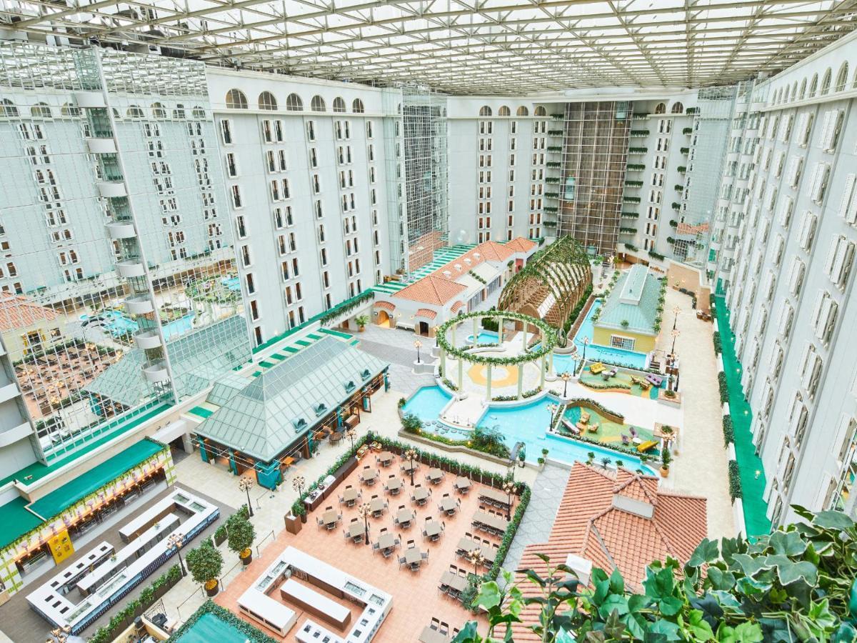 Grand Nikko Tokyo Bay Maihama Hotell Urayasu Exteriör bild The photo depicts a large indoor area, likely within a resort or hotel, featuring a spacious atrium. The atrium has a glass roof, allowing natural light to flood the space. In the center, there are various swimming pools and a lush, green landscape w