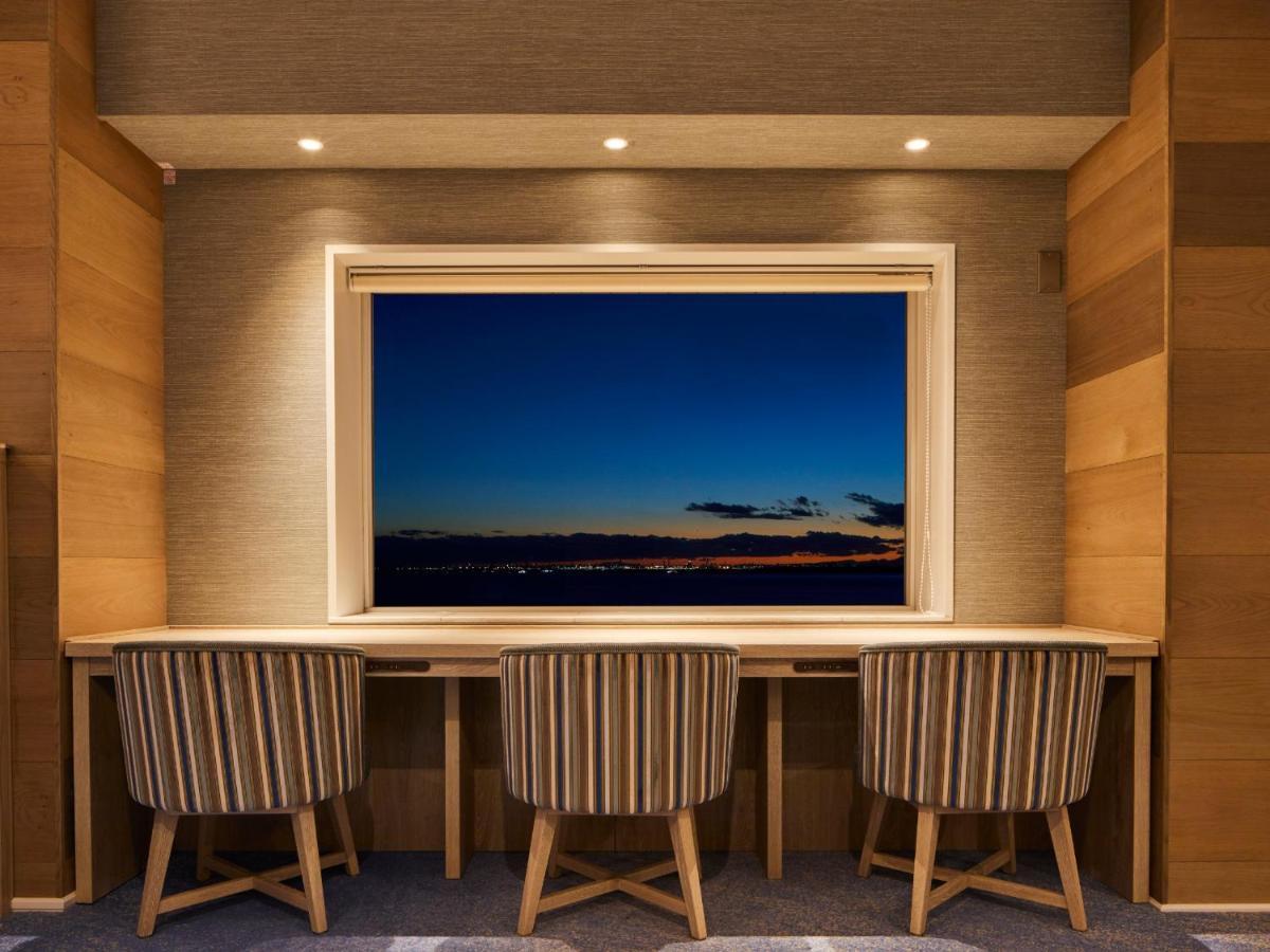 Grand Nikko Tokyo Bay Maihama Hotell Urayasu Exteriör bild The photo depicts a cozy workspace or study area featuring a long, minimalist desk with three chairs. The wall behind the desk is made of wood, creating a warm atmosphere. At the center, there is a large window that showcases a beautiful evening view