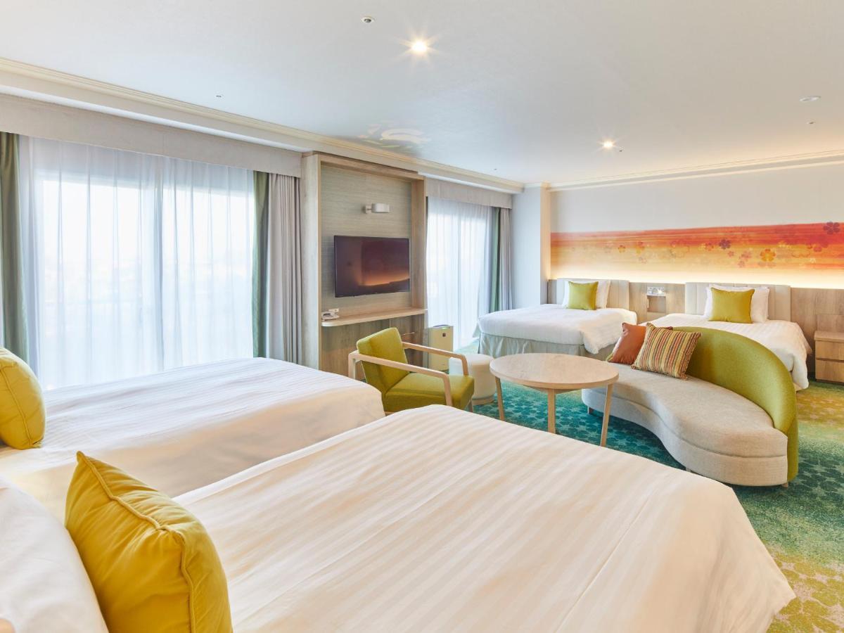 Grand Nikko Tokyo Bay Maihama Hotell Urayasu Exteriör bild The photo shows a modern hotel room that features two large beds covered with white bedding and decorative pillows. There is a contemporary, curved sofa in a light color, along with a round table in the middle. The room has large windows that allow n