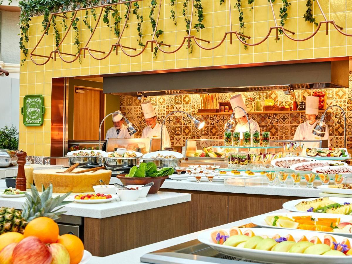 Grand Nikko Tokyo Bay Maihama Hotell Urayasu Exteriör bild The photo shows a vibrant and colorful buffet setup in a restaurant. In the foreground, there are various dishes arranged on white platters, featuring an assortment of fruits, desserts, and other items. The background features chefs in white uniforms