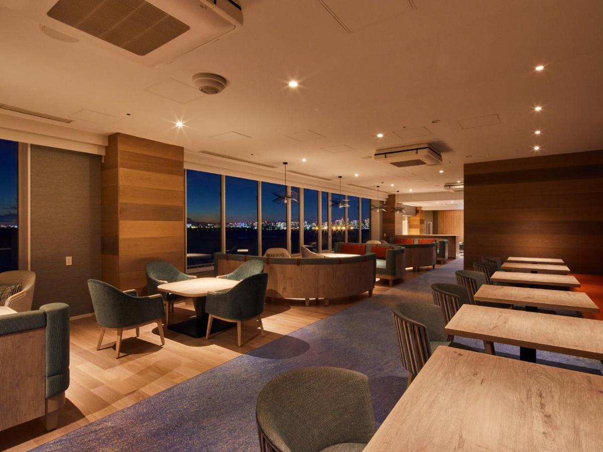 Grand Nikko Tokyo Bay Maihama Hotell Urayasu Exteriör bild The photo shows a modern, well-lit lounge or café area. It features a mix of seating options, including cozy armchairs and tables with chairs. The space has large windows displaying a view, likely of a city or landscape at dusk, given the nighttime a