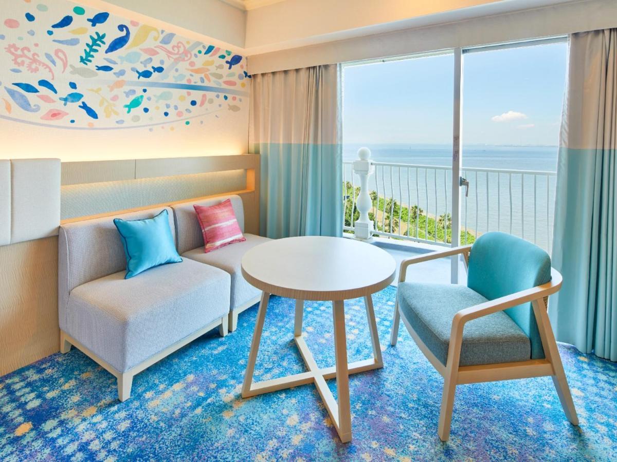 Grand Nikko Tokyo Bay Maihama Hotell Urayasu Exteriör bild The photo shows a modern and stylish interior of a room with a view. There is a cozy seating area featuring a light-colored sofa with decorative cushions in various shades of blue and pink. A round table occupies the center of the space, surrounded b