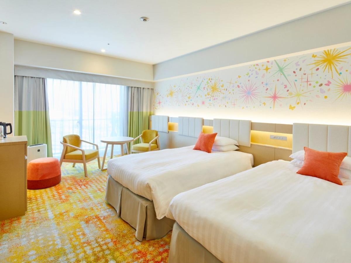 Grand Nikko Tokyo Bay Maihama Hotell Urayasu Exteriör bild The photo shows a modern hotel room featuring two twin beds with light-colored bedding and decorative orange cushions. There is a vibrant, colorful carpet on the floor, and the walls are adorned with playful designs, including bursts of color. A larg