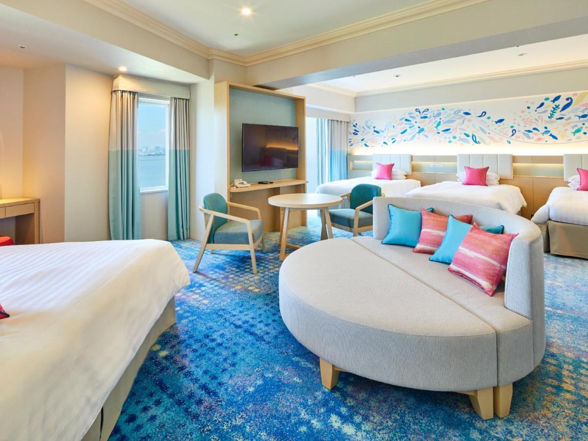 Grand Nikko Tokyo Bay Maihama Hotell Urayasu Exteriör bild The photo shows a modern hotel room featuring a spacious layout with multiple beds. There is a large, curved sofa with colorful cushions in the center, adding a contemporary touch to the design. The room has large windows allowing natural light to fi
