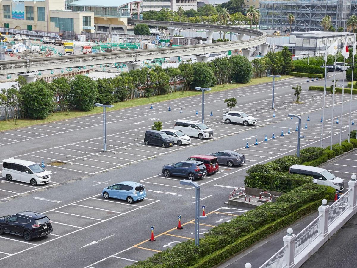 Grand Nikko Tokyo Bay Maihama Hotell Urayasu Exteriör bild The photo shows a partially empty parking lot with several parked cars. In the foreground, there are a few vehicles, including a blue car and a white one. The lot has clearly marked parking spaces, and there are some trees and shrubs along the sides.