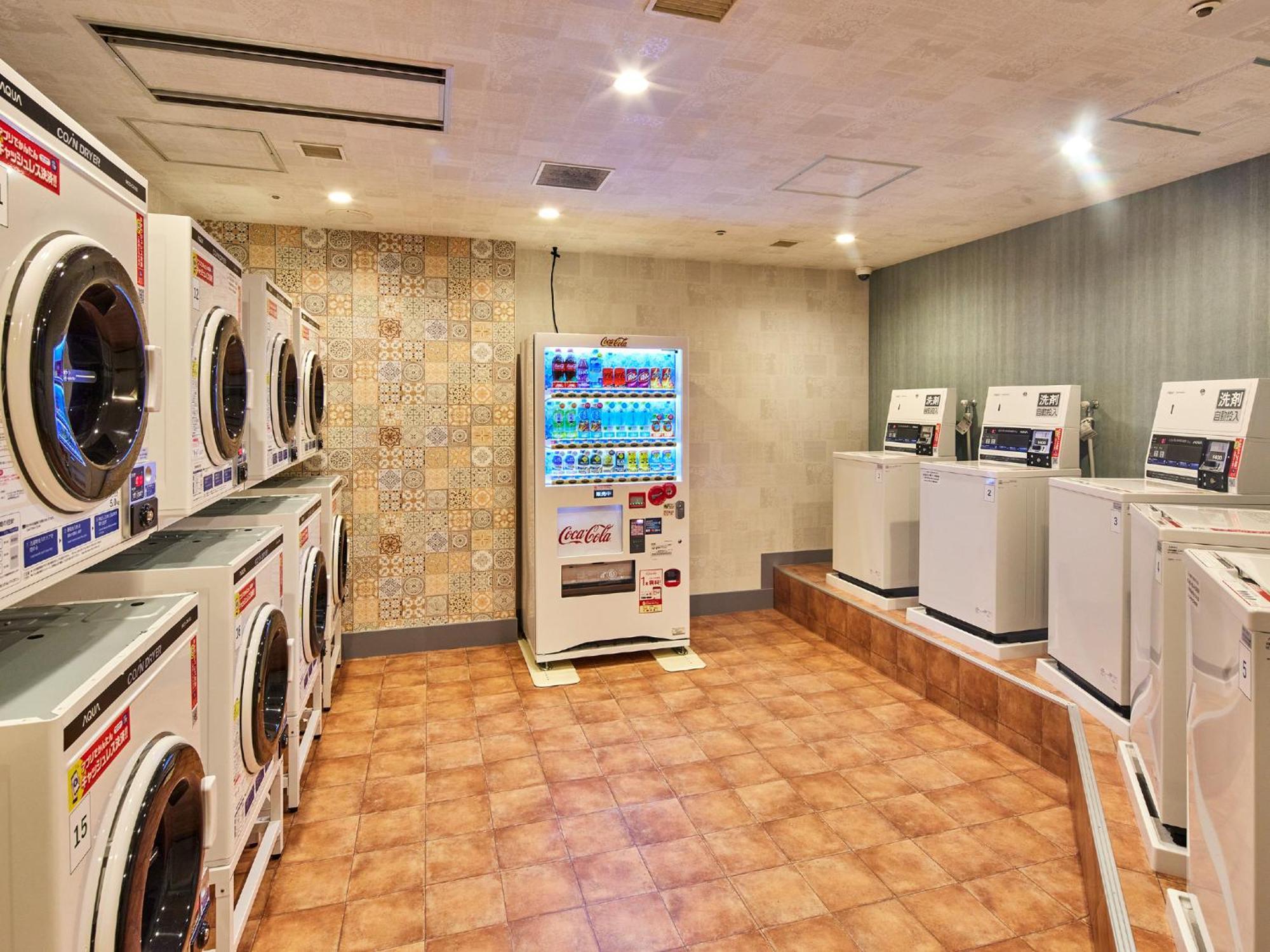 Grand Nikko Tokyo Bay Maihama Hotell Urayasu Exteriör bild The photo shows a laundry room equipped with several washing machines and dryers. On the left side, there are multiple front-loading washing machines arranged in a row, and on the right side, there are dryers. In the center, there is a vending machin